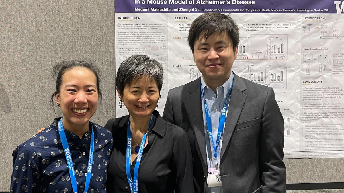 Three people stand together in front of a research poster smiling.