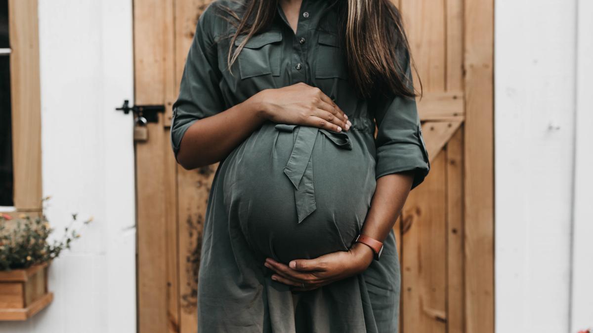 A woman cradles her pregnant belly in front of a wooden door.