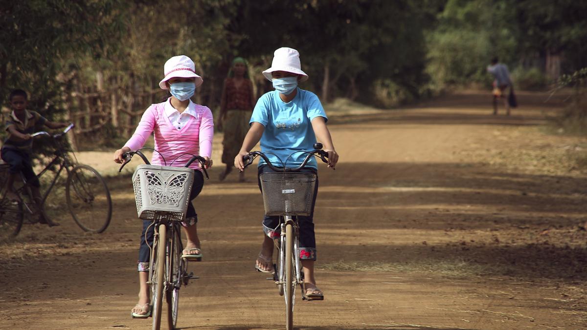 Two women wearing air masks on bicycles on a dirt road.
