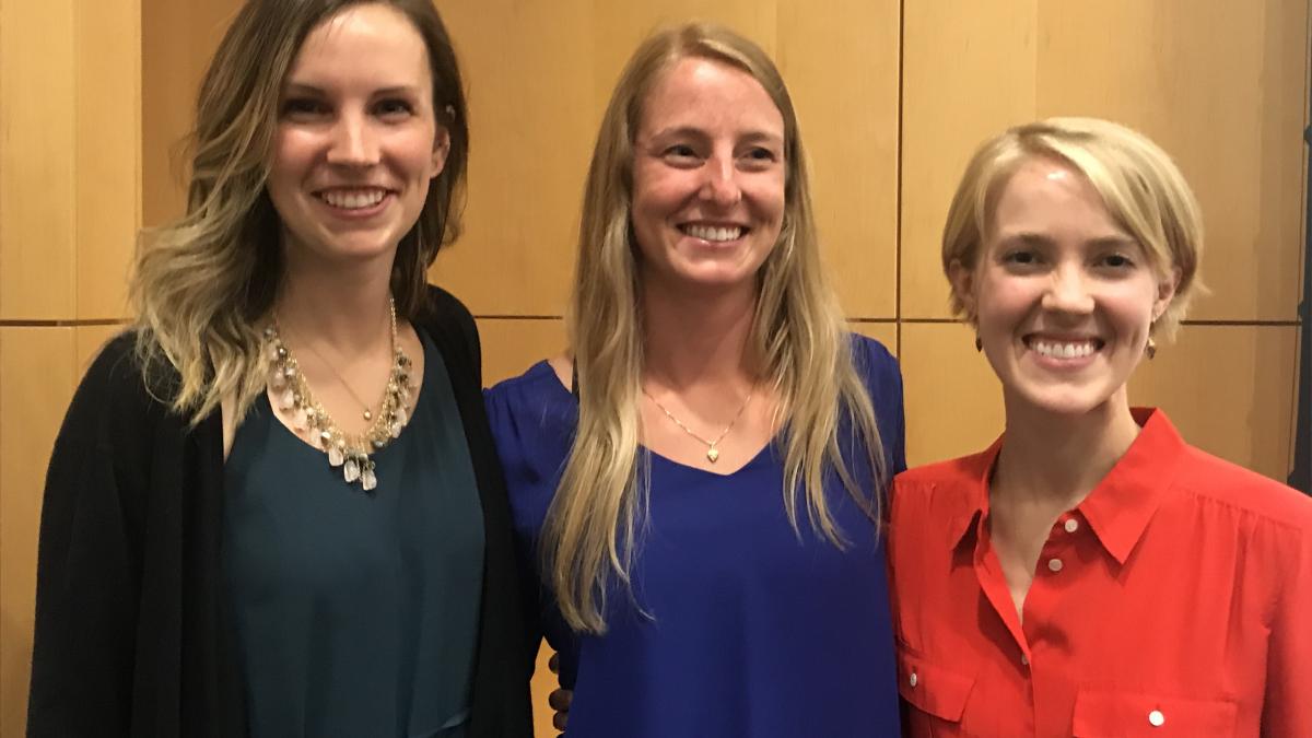 Three DEOHS students smiling with their arms around one another.