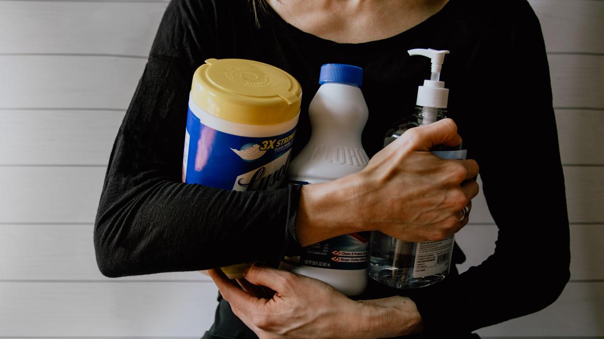 A woman dressed in a black shirt holds several cleaning products in her arms.