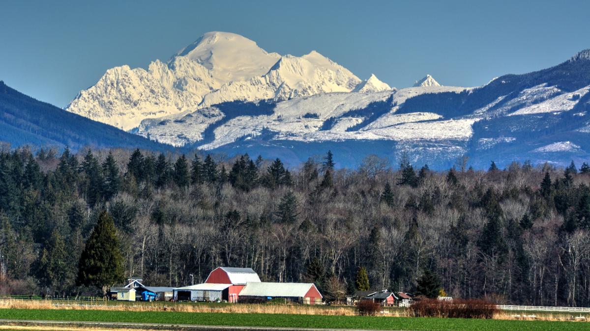 A red barn and farmland in the foreground with Mount Baker in the background.