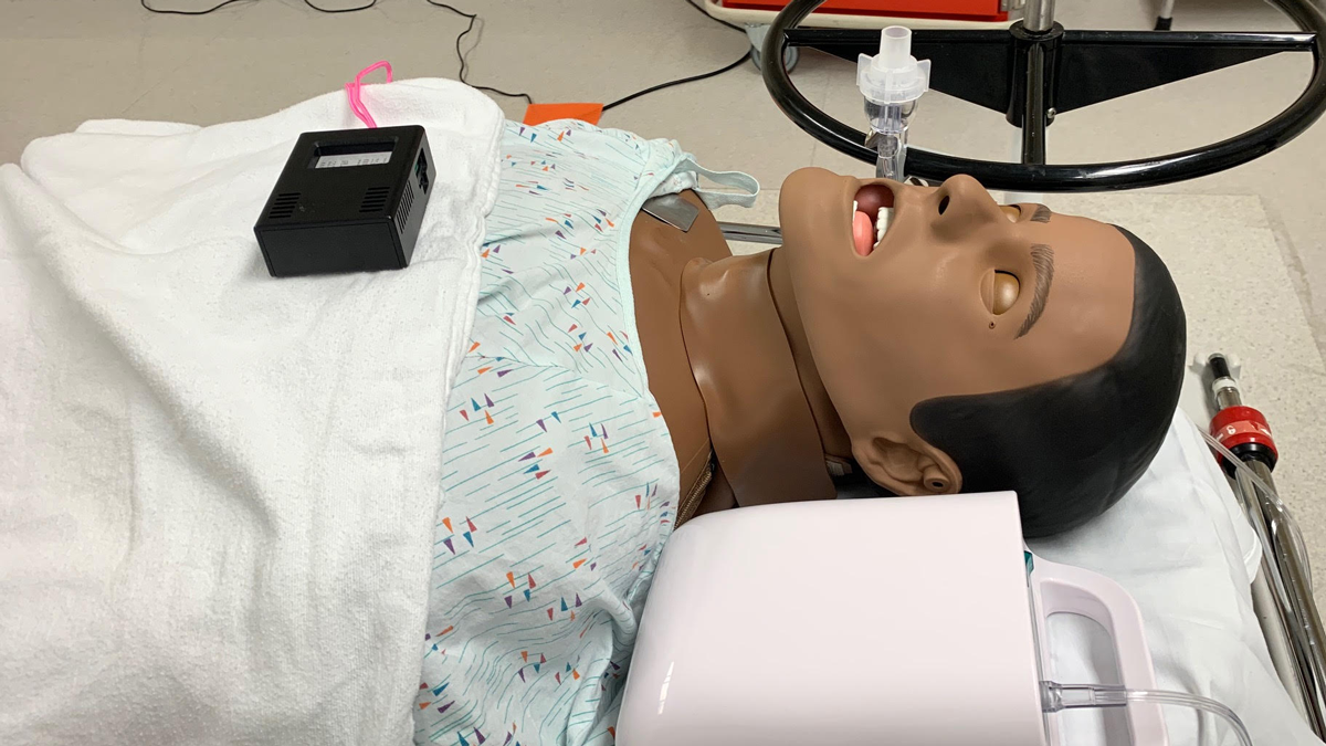 A mannequin on an operating table with a black air monitoring sensor on its chest.