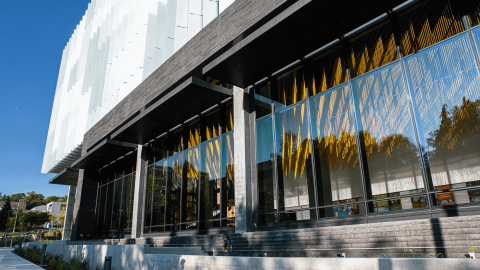 Outside view of the UW Hans Rosling Building, a glass and steel building with a sculpture of hanging gold threads in the lobby.