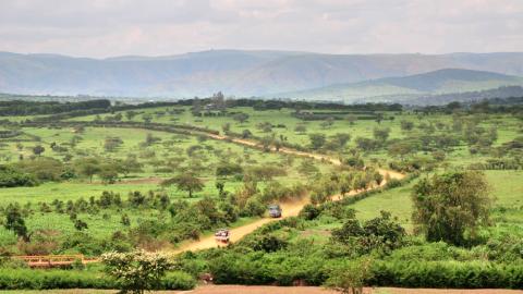 A landscape shot of two vehicles traveling along a dirt road through a hilly area of rural Rwanda.