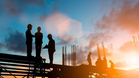 Construction workers in silhouette working on the top of a building.
