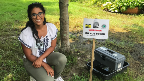 A woman kneels on a grassy lawn next to health department signage.