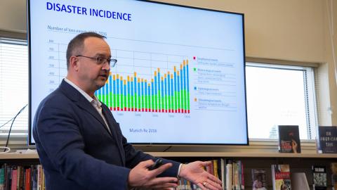 A man stands in front of a screen projecting a slide with the title "Disaster incidence."