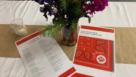 A table with a vase of flowers, a candle, and some printed materials on preventing sexual harassment in agriculture.