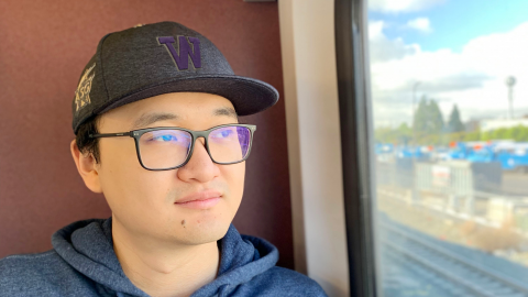 Man with a University of Washington baseball cap on looking out the window of a train.