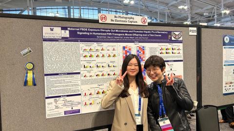 Sarah Kim and Julia Cui stand in front of Sarah's research poster while throwing up peace signs.