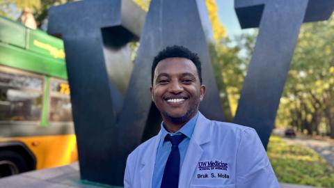 Bruk Molla stands in a white doctor's coat in front of the UW "W" sculpture.
