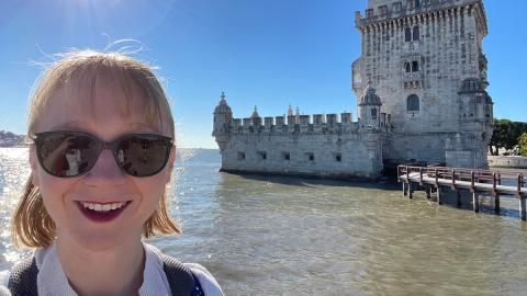 Photo of Sarah Philo in sunglasses standing in front of a body of water and Portugal's Belém Tower.