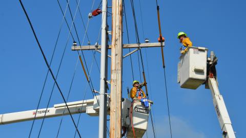 Utility workers in cherry pickers work on electrical power lines.