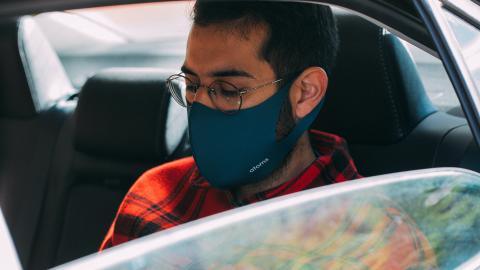A man wearing a face mask sits in the back seat of a car.