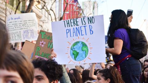Close-up on youth marching for climate action, with a sign with text "There is No Planet B" and a drawing of the Earth with bright lines surrounding it.