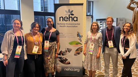 Six people stand around a sign for the National Environmental Health Association.