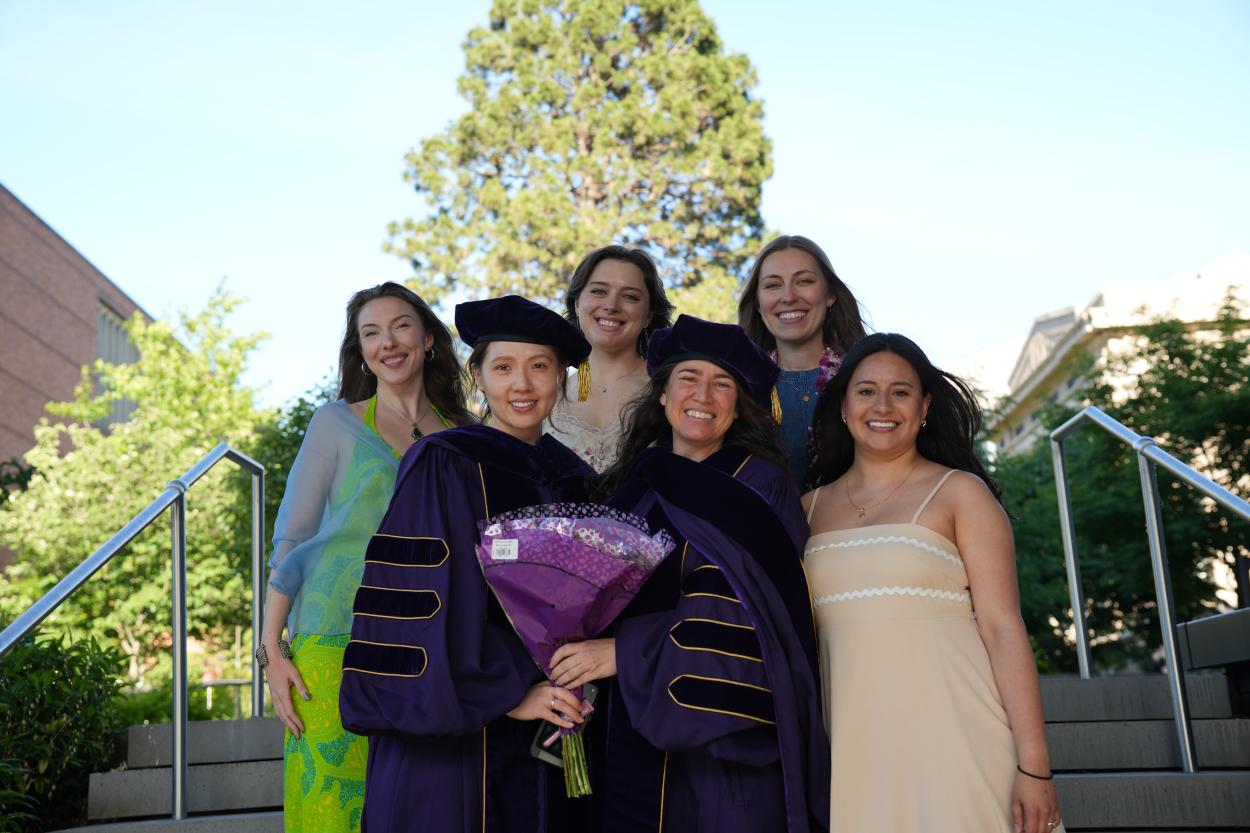 A group of PhD graduates stands together outside to celebrate their graduation.