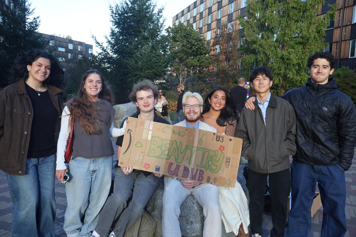 Seven people including Emily Do stand together on the UW campus holding a sign reading "Beautify U Dub"