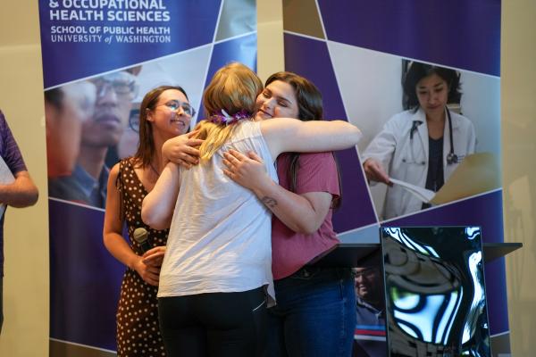 Emily Hovis hugs Grace Hively on a stage while Mariah Rubin smiles.