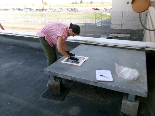 Rachel Sklar leans over an outdoor platform at a corrections facility to take a wipe sample.