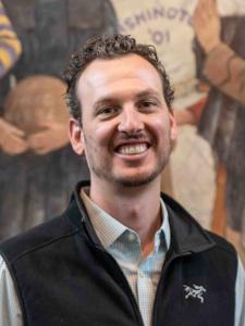 Dr Peckham, a young white man with curly brown hair and a beard