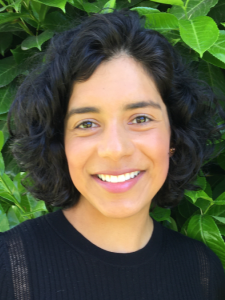 Woman with black hair and black sweater against green leafy background