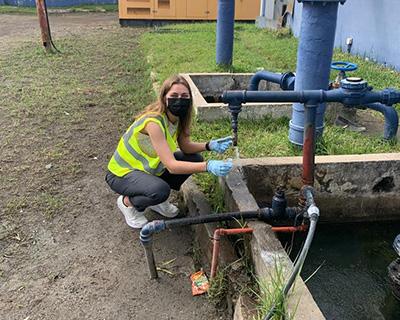 Becky Kann crouches down near a water pipe to take a water sample.