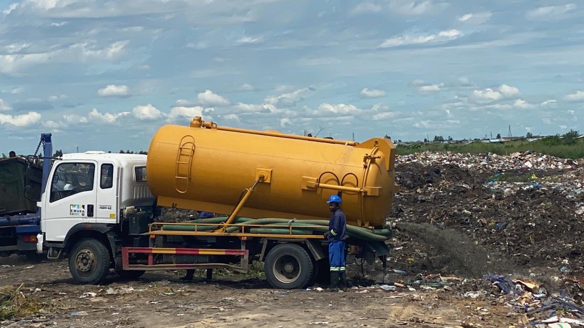 A truck with a large yellow tank empties fecal sludge at a waste site.