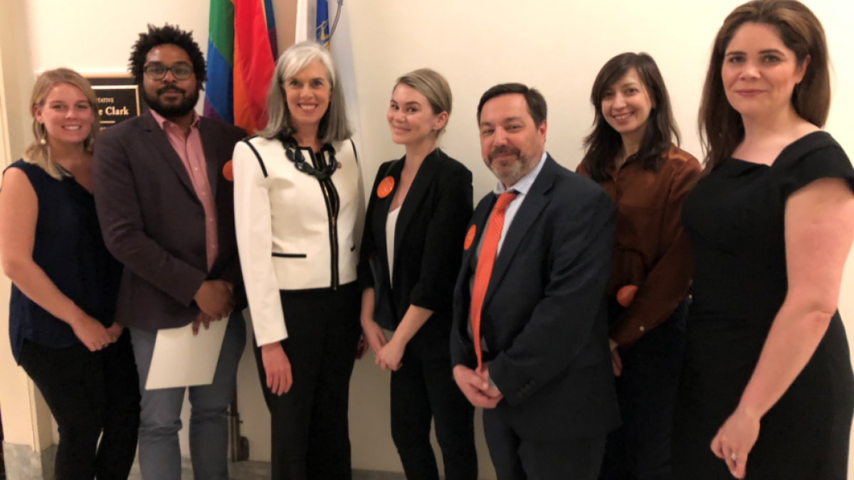 A row of researchers in dark clothes stand with Representative Katherine Clark (D-MA)