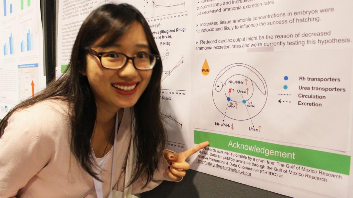 Dr. Wang leans forward next to a conference poster presenting results from her dissertation research.