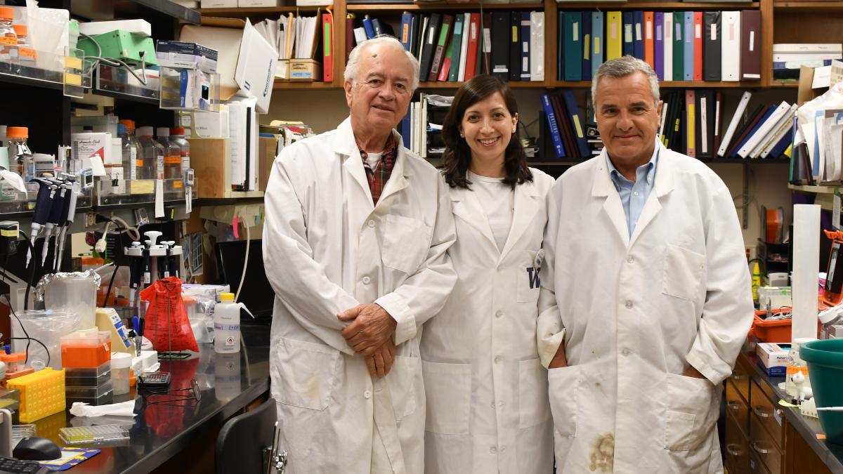 Three reserachers in white lab coats stand in a lab.