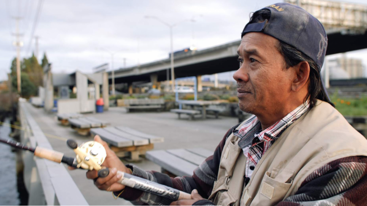 A fisher holds a rod on a dock by the Duwamish River