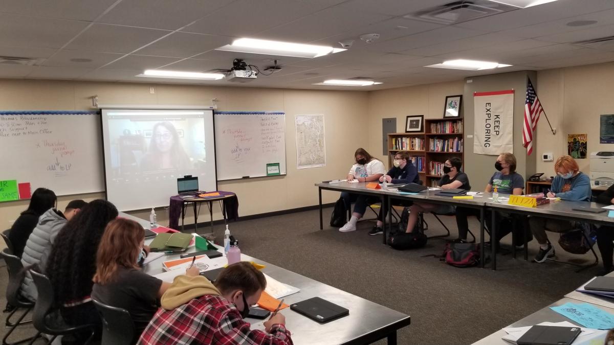 BJ Cummings is displayed on a large monitor at the front of a classroom full of high school students. 