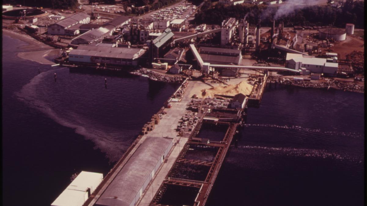 A historic aerial photo of the Royonier Paper Mill facility jutting into Port Angeles Harbor 